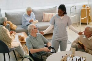 Resident sitting with a small dog in a bright assisted living apartment beside a pet bed and water bowl