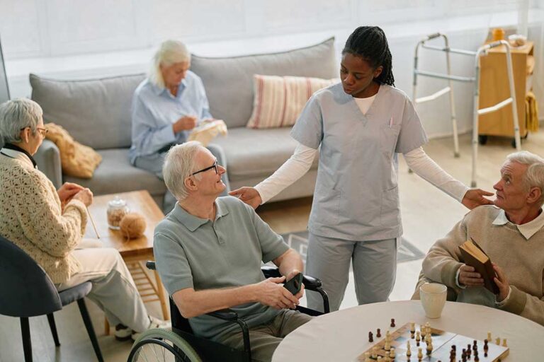 Resident sitting with a small dog in a bright assisted living apartment beside a pet bed and water bowl