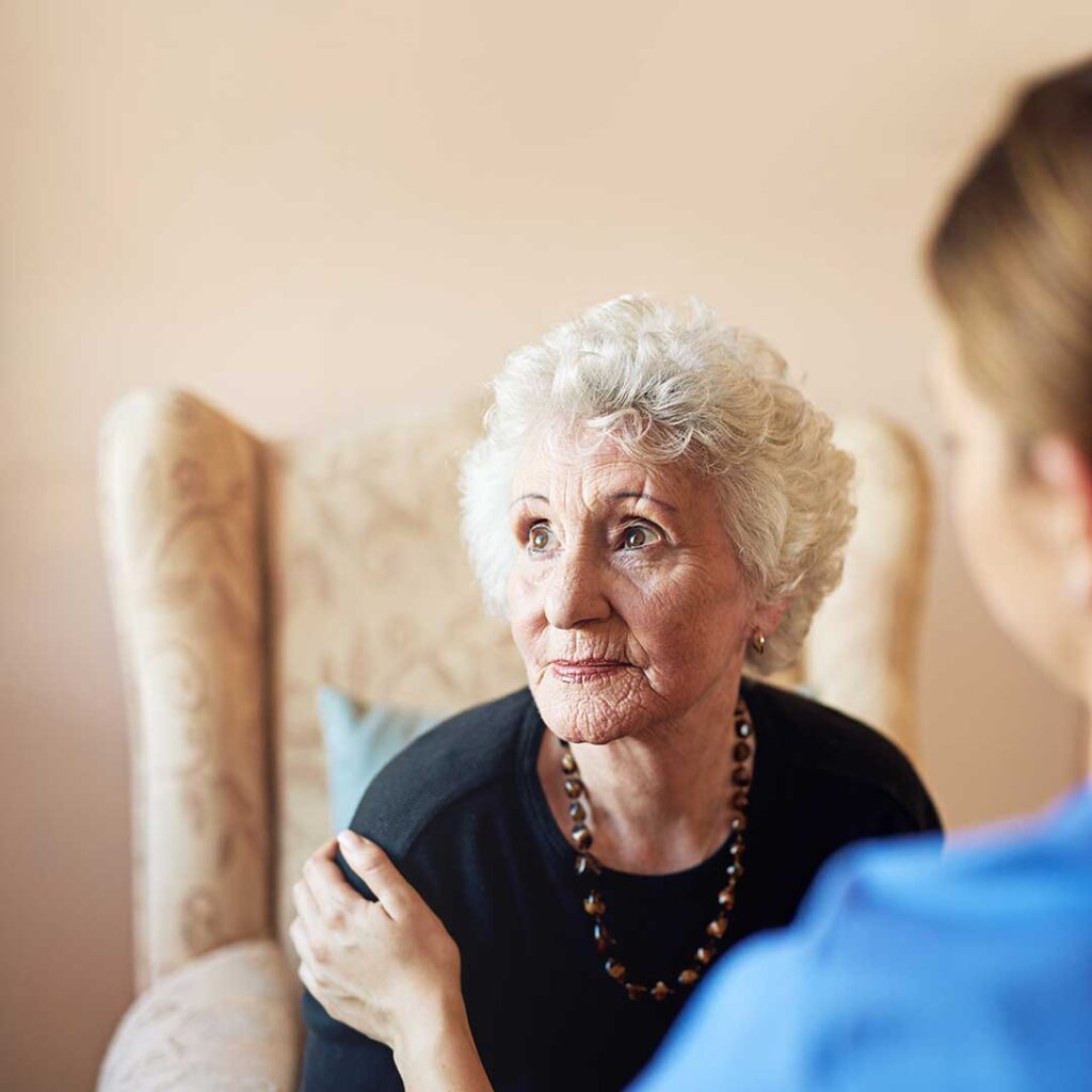 A caregiver assisting an older adult with daily activities inside a bright, comfortable living space.