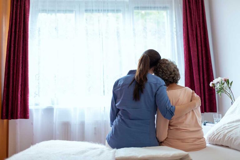 Family member listens to an older adult in a warmly furnished assisted living room.